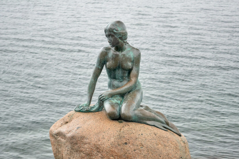 Kleine Meerjungfrau in Kopenhagen auf einem Felsen am Ufer sitzend, mit Blick auf das ruhige Wasser