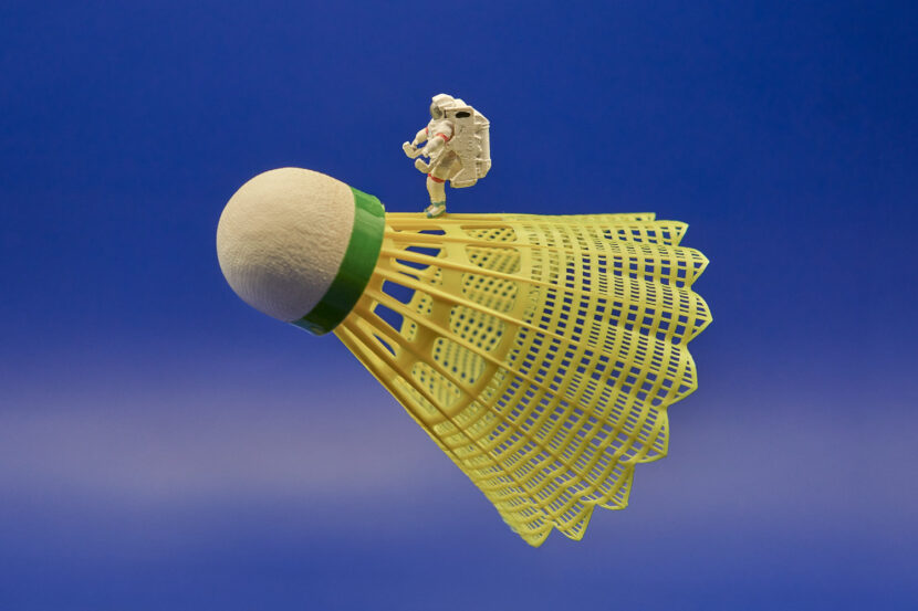 Dies ist ein Bild mit Miniaturfiguren. Zu sehen ein leicht nach oben geneigter Badminton-Federball, auf dem ein Astronat steht. Das Motiv ist von der Seite aufgenommen. Die Bildanordnung sieht ein wenig aus wie eine startende Rakete.