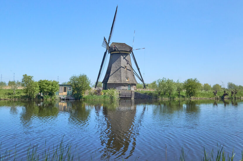 Historische Windmühle in Kinderdijk am Wasser, mit Spiegelung im Kanal unter klarem blauem Himmel