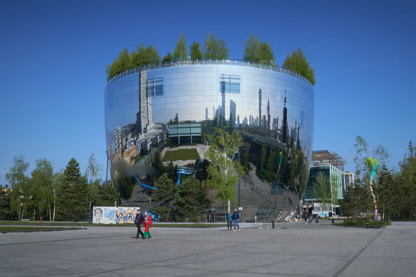 Das spiegelnde Depot des Museum Boijmans Van Beuningen in Rotterdam ragt futuristisch in den Himmel. Die runde Glasfassade reflektiert Stadt, Menschen und den blauen Himmel.