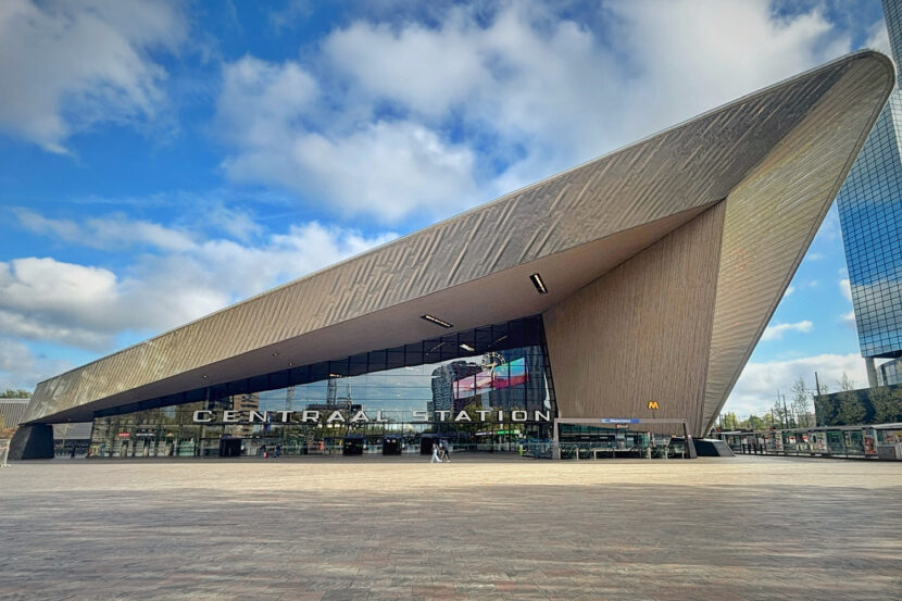 Die moderne Centraal Station in Rotterdam beeindruckt mit ihrer markanten, spitz zulaufenden Architektur. Vor dem Gebäude öffnet sich ein weiter Platz unter blauem Himmel mit Wolken.