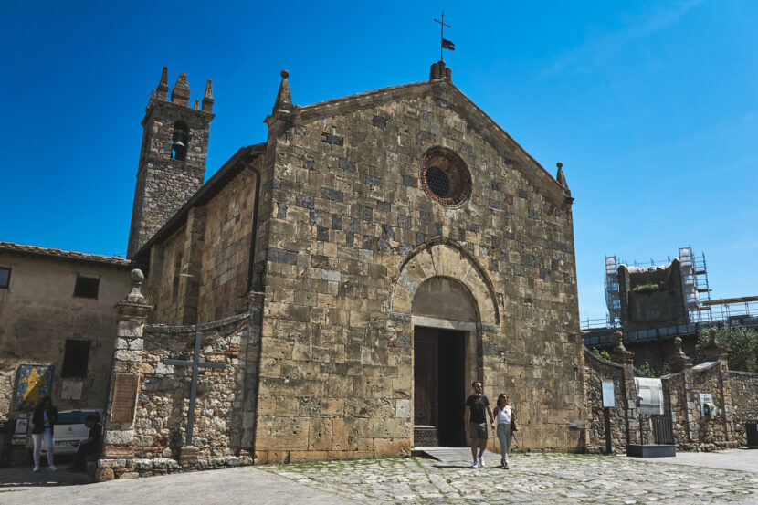 Historische Kirche im mittelalterlichen Monteriggioni mit Natursteinfassade unter strahlend blauem Himmel