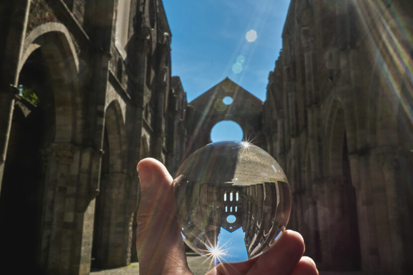 Glaskugel vor der Abbazia di San Galgano, die die beeindruckenden Bögen der Dachruine gespiegelt zeigt
