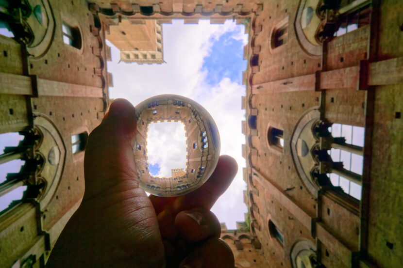 Blick durch den Innenhof des Palazzo Pubblico in Siena, gespiegelt in einer Glaskugel vor blauem Himmel