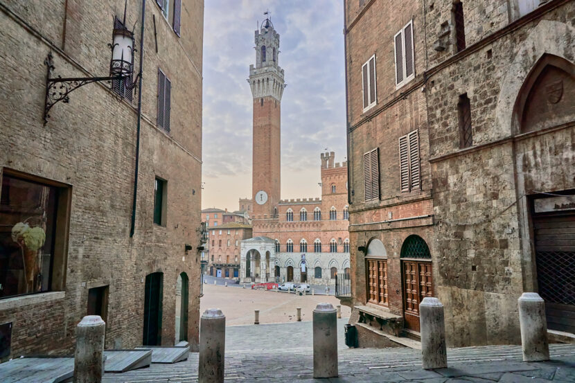 Blick durch eine historische Gasse in Siena auf den Torre del Mangia und den Palazzo Pubblico an der Piazza del Campo