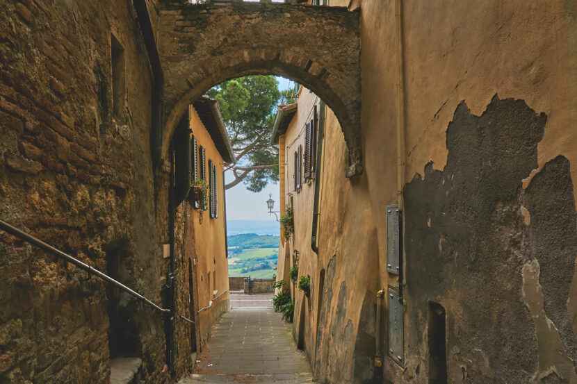 Historische Gasse in Montepulciano mit Natursteinbogen und Blick auf die sanfte Hügellandschaft der Toskana