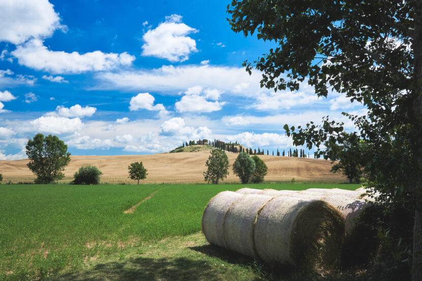 Sanfte Hügellandschaft der Crete Senesi mit Heuballen, Zypressen und weitem Himmel voller Wolkenformationen